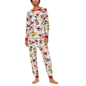 A person wearing a matching pajama set featuring a colorful print of classic Disney characters, including Mickey Mouse and friends, with red cuffs and neckline.