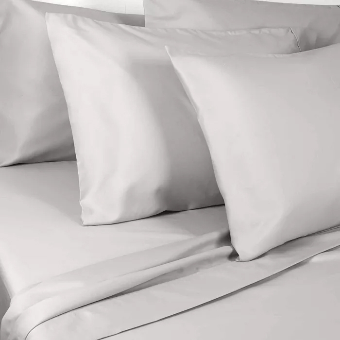 Light gray pillow and bed sheets set comprising multiple pillows and a flat sheet on a neatly made bed.