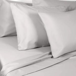 Light gray pillow and bed sheets set comprising multiple pillows and a flat sheet on a neatly made bed.