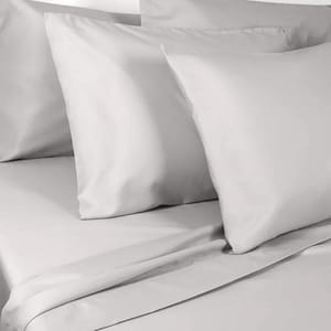 Light gray pillow and bed sheets set comprising multiple pillows and a flat sheet on a neatly made bed.