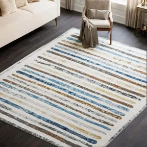 A modern living room features a rug with horizontal stripes in blue, brown, and beige tones, placed on a dark wooden floor. A beige sofa and armchair add to the decor, providing a contemporary and cozy atmosphere.