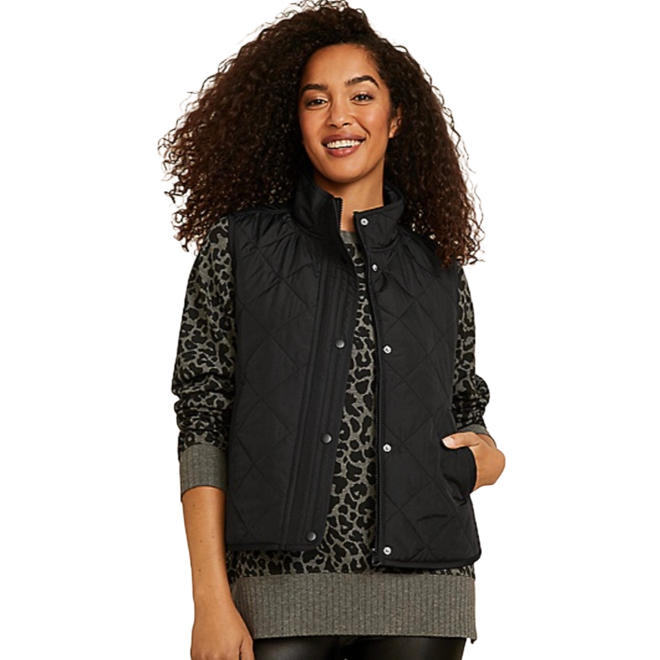 A woman is wearing a black quilted vest over a leopard print sweater.