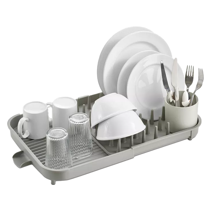 Expandable dish drying rack with a gray base holding white plates, bowls, mugs, and clear glasses. Includes a cutlery compartment with forks, spoons, and knives.