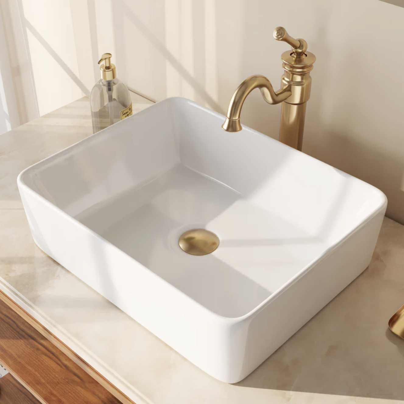 A rectangular white sink with a gold circular drain is set on a marble countertop. Nearby, a gold faucet and a clear soap dispenser with a pump are visible.