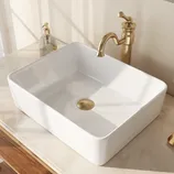 A rectangular white sink with a gold circular drain is set on a marble countertop. Nearby, a gold faucet and a clear soap dispenser with a pump are visible.