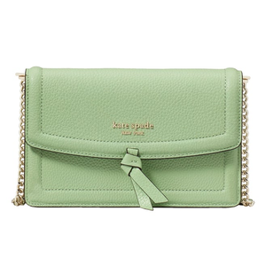 A light green Kate Spade Leather Knott Crossbody features a textured finish, a flap closure with a bow detail, and a gold chain strap. The brand's logo is displayed on the front.
