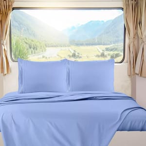 A bed with light blue sheets and pillowcases is placed against a large window overlooking a mountainous landscape. Light beige curtains frame the window.