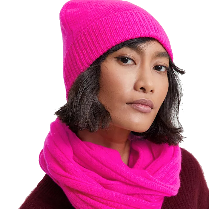 A bright pink beanie made from 100% cashmere, featuring a cuffed design for added warmth and style. It pairs well with winter outfits, offering a soft and luxurious feel.