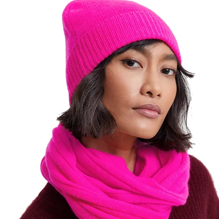 A bright pink beanie made from 100% cashmere, featuring a cuffed design for added warmth and style. It pairs well with winter outfits, offering a soft and luxurious feel.