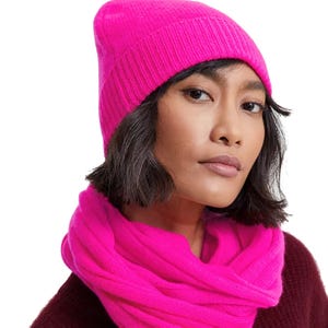 A bright pink beanie made from 100% cashmere, featuring a cuffed design for added warmth and style. It pairs well with winter outfits, offering a soft and luxurious feel.