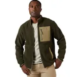 A man wears an olive green fleece jacket with khaki trim and zippered chest and side pockets, paired with a light beige shirt and pants.