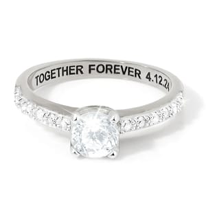A silver ring with a central round diamond and smaller diamonds on the band, engraved with \“TOGETHER FOREVER 4.12.24\“ on the inner side.