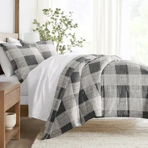 A bed with a black and gray plaid comforter set, including matching pillow shams, is shown in a bright, minimalistic bedroom with a wooden side table and a potted plant for decoration.