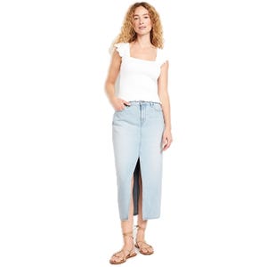 A woman is wearing a white square-neck top with ruffled sleeves, a light blue denim midi skirt with a front slit, and tan strappy sandals.