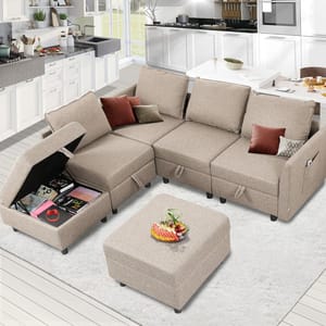 A beige modular sectional sofa with hidden storage in one seat and an ottoman topped with fruit. The living room includes a modern kitchen in the background.
