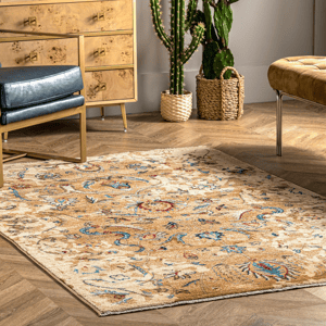 A beige and colorful patterned rug is placed on a wooden herringbone floor, accompanied by a wooden dresser, a black leather chair, and a cactus in a woven basket.
