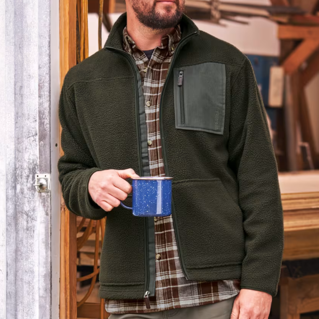 The RedHead Berber Fleece Jacket features a dark green, textured fleece with a front zipper, zippered chest pocket, and two side pockets. It's worn over a plaid shirt and is paired with a blue speckled mug.