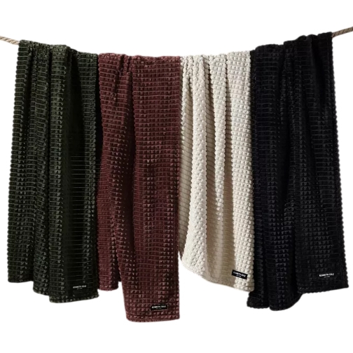 Kenneth Cole Jacquard Plush Throws are displayed in four colors: green, red, white, and black. They feature a textured, waffle-like pattern, perfect for adding a cozy touch to any space.