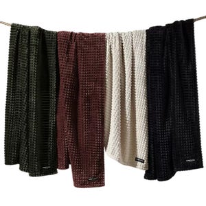 Kenneth Cole Jacquard Plush Throws are displayed in four colors: green, red, white, and black. They feature a textured, waffle-like pattern, perfect for adding a cozy touch to any space.
