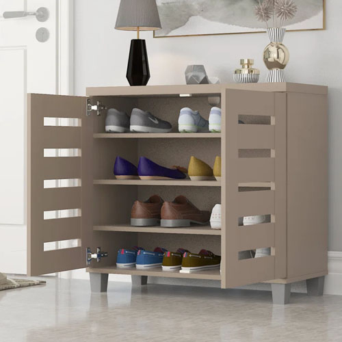 A beige shoe cabinet with multiple shelves displaying various pairs of shoes, located in a modern interior setting with decorative items on top.