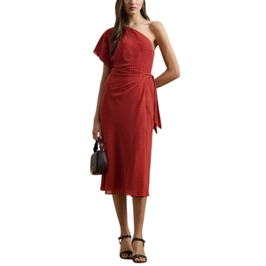 A woman is wearing a one-shoulder red polka dot midi dress with a tie waist, paired with black heeled sandals and holding a small black handbag.