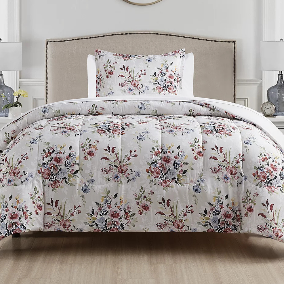 Floral-patterned comforter and pillowcase set on a neutral-toned bed, complemented by a simple headboard, with two table lamps and decorative items in the background.