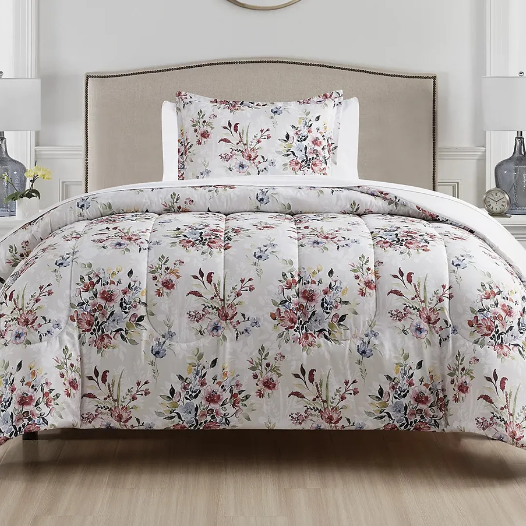 Floral-patterned comforter and pillowcase set on a neutral-toned bed, complemented by a simple headboard, with two table lamps and decorative items in the background.