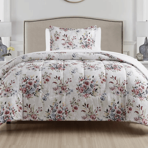 Floral-patterned comforter and pillowcase set on a neutral-toned bed, complemented by a simple headboard, with two table lamps and decorative items in the background.