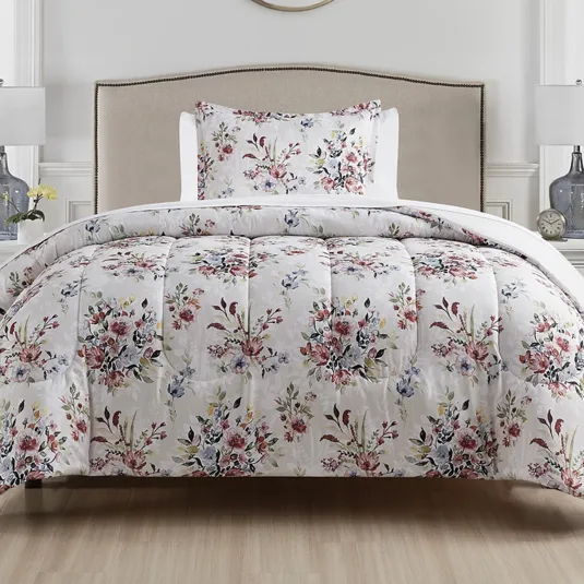 Floral-patterned comforter and pillowcase set on a neutral-toned bed, complemented by a simple headboard, with two table lamps and decorative items in the background.