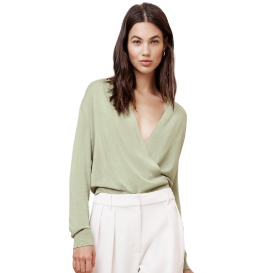 A woman wearing a pale green wrap-style top paired with white trousers.