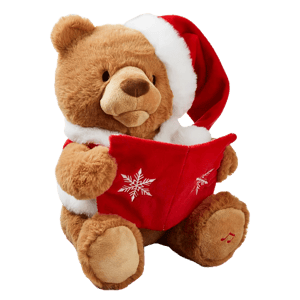 A plush bear wearing a Santa hat and red coat holds a red book with snowflake designs. It appears to be an animated toy designed for storytelling, featuring a music note emblem on its paw.