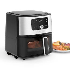 Cuisinart air fryer with a digital display and control knob, showing food being cooked inside. A plate with cooked salmon and vegetables is visible next to it.