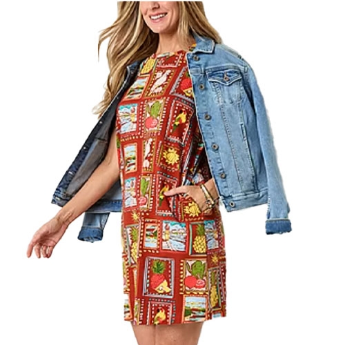 A woman is wearing a colorful patch-pattern dress with fruit and beach designs, paired with a blue denim jacket draped over her shoulders.