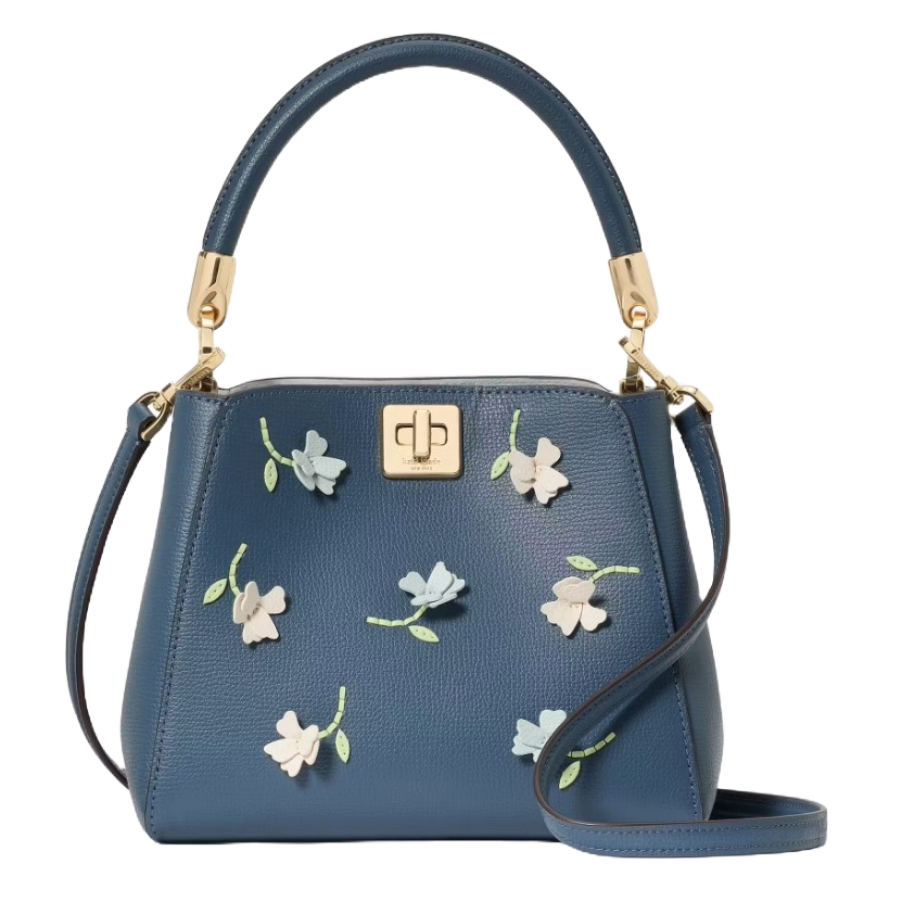 A blue Kate Spade crossbody bag featuring floral appliques with gold-tone hardware, a top handle, and a detachable strap, along with a central turn-lock closure.