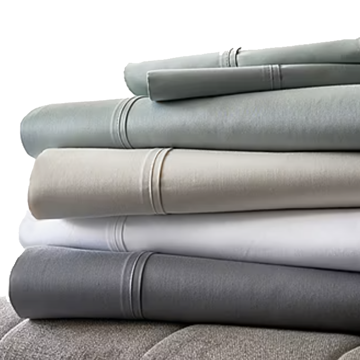 A stack of folded bedsheets in various colors, including gray, beige, white, and light blue, with decorative stitching near the edges.