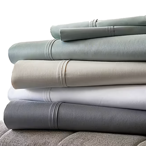 A stack of folded bedsheets in various colors, including gray, beige, white, and light blue, with decorative stitching near the edges.