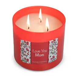 Red, three-wick candle labeled \“Love You Mom\“ with a floral border, scented with rose petals and velvet woods.