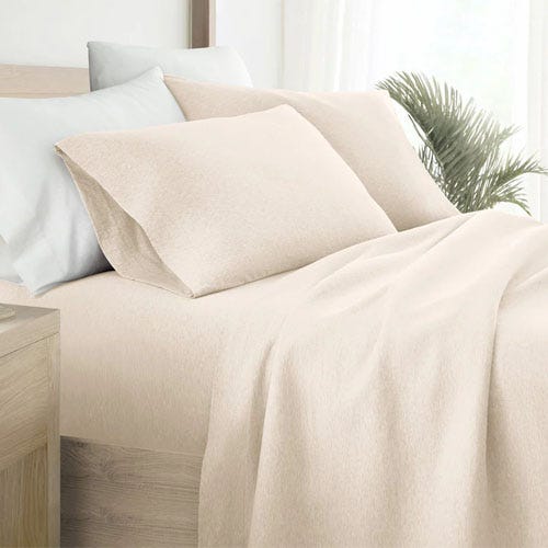 A beige bedding set with a fitted sheet, top sheet, pillowcases, and a comforter on a bed.