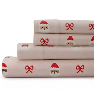 A stack of queen-sized sheets in a light pink color, featuring a festive pattern with Santa faces and red ribbons.