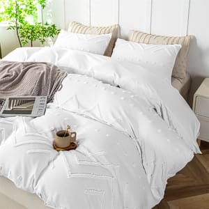 A white queen comforter set with decorative tufts and textured geometric patterns, accompanied by matching pillowcases and a beige throw blanket at the foot of the bed.