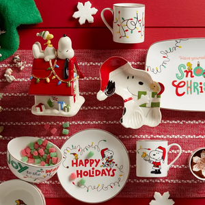 A collection of holiday-themed tableware featuring Snoopy and other Peanuts characters, including plates, mugs, and a candy dish.