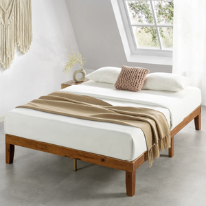 A wooden platform bed with a white mattress, beige knit throw, and two white pillows is displayed in a minimalistic room with a sloped ceiling and a decorative wall hanging.
