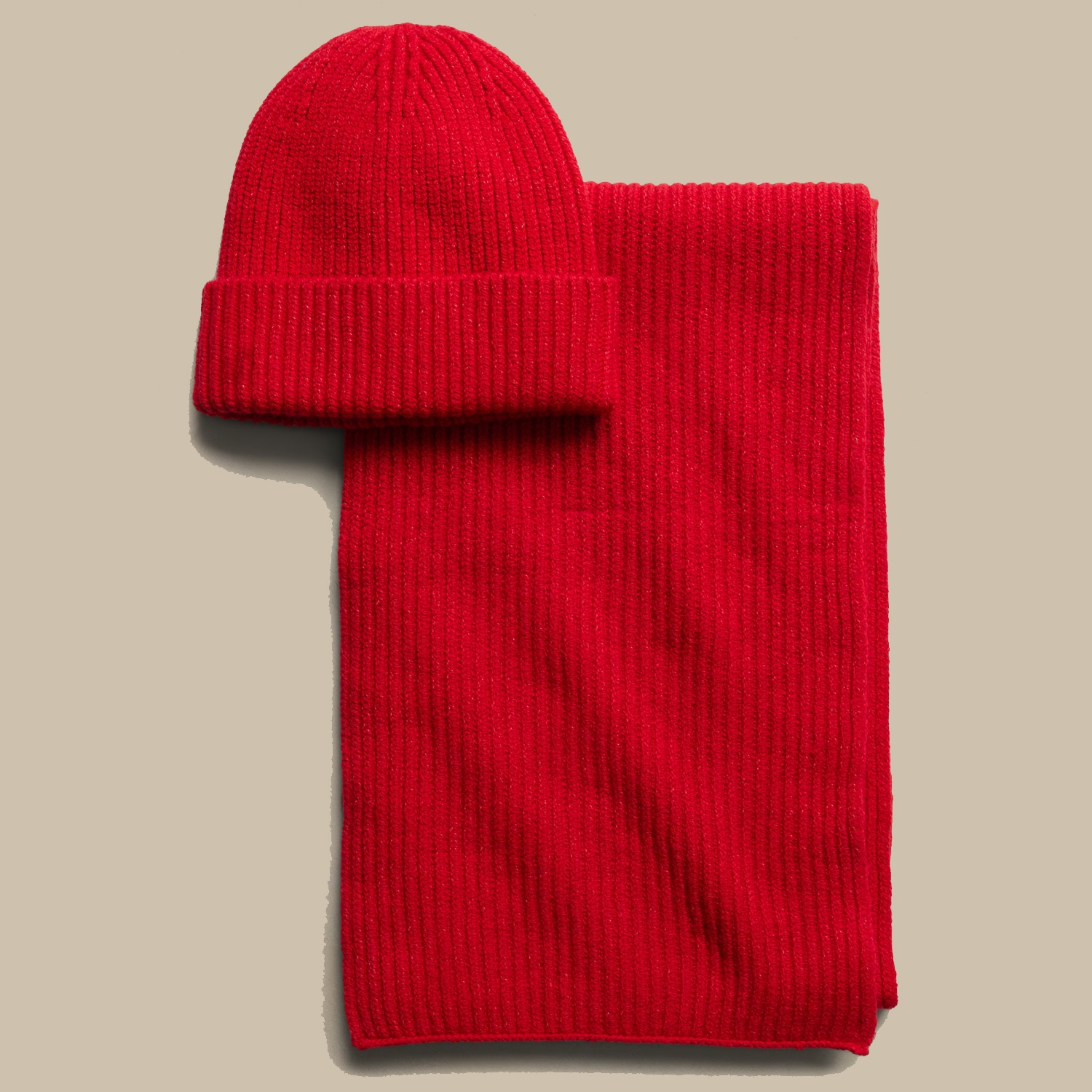 Red knitted beanie alongside matching scarf on a beige background.