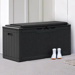 A black storage box is placed on a porch next to a wooden door, accompanied by a pair of white boots. House numbers \“4028\“ are seen on the wall, and a copper light fixture hangs above.