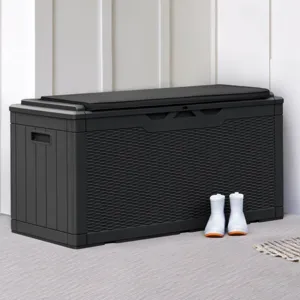 A black storage box is placed on a porch next to a wooden door, accompanied by a pair of white boots. House numbers \“4028\“ are seen on the wall, and a copper light fixture hangs above.