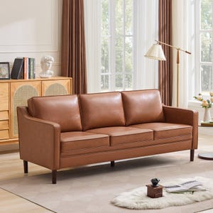 A brown leather sofa with three cushions is placed in a living room setting, featuring a wooden sideboard, a floor lamp, and a plush rug on a light-colored floor.