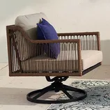 A swivel outdoor armchair with wicker sides, beige cushions, and a blue throw pillow.