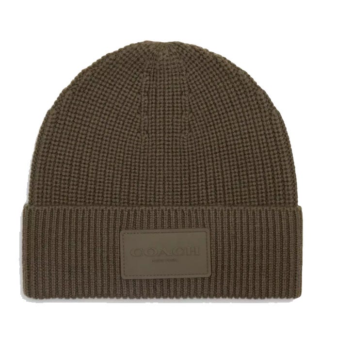 A brown Coach knit beanie featuring a ribbed design with a fold-over cuff and a prominent rubber patch displaying the Coach logo.
