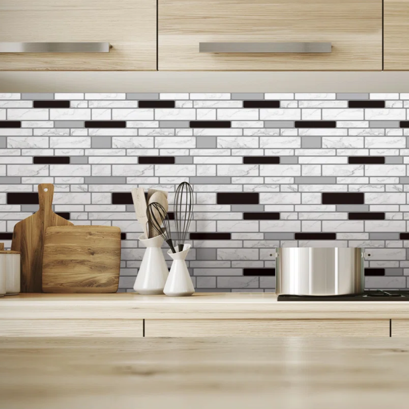Modern kitchen features a black and white mosaic tile backsplash with wooden cabinets. A stainless steel pot, wooden cutting boards, whisks, and a potted plant are on the countertop.