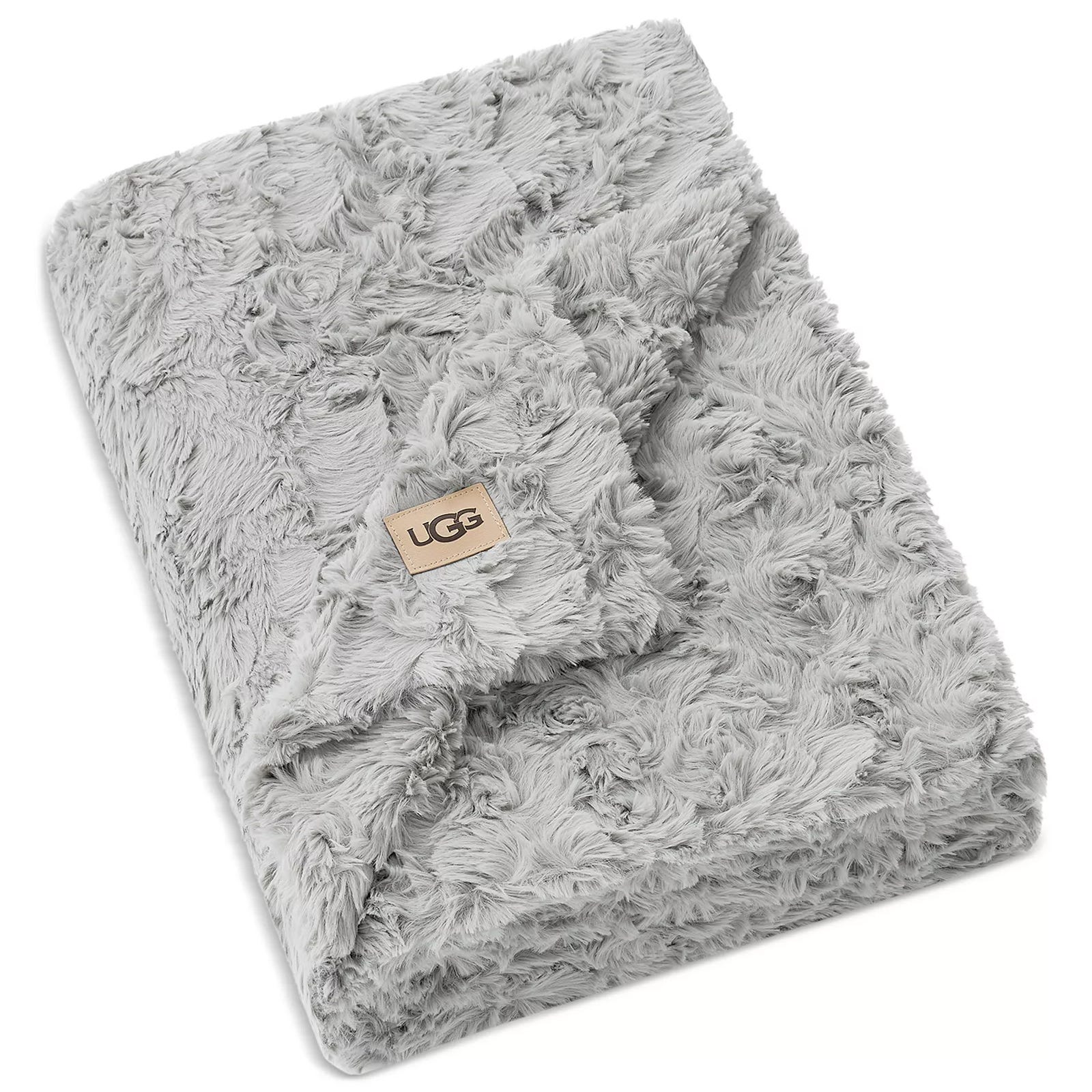 A soft, grey faux fur blanket with the UGG logo on a tan patch, featuring a textured, plush design.